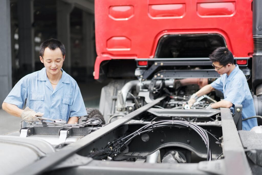Two male factory workers teamworking on truck at crane factory, China